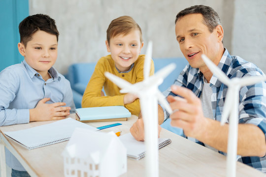 Interesting information. Pleasant upbeat father pointing at the wind turbine models standing on his table and discussing their construction with his curious sons