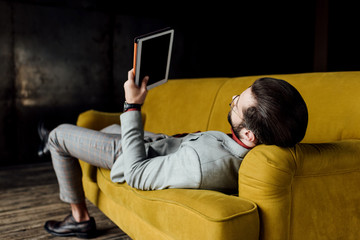 man using digital tablet while lying on couch