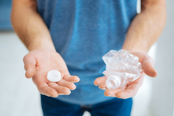 Harmful plastic. The focus being on the hands of a man in a blue t-shirt holding a crushed plastic bottle, ready for recycling