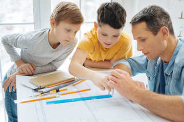 Easy lesson. Curious pre-teen boys leaning over their fathers work desk and learning how to use the compass while their father teaching them to do so