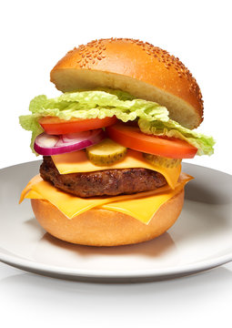 Hamburger with cheese, pickles, tomato, onions, lettuce on plate