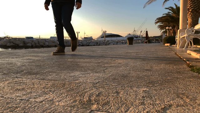 Young man in casual clothes walking on stone shore in port on cold sunny winter day slow motion