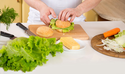 Close-up of male hands preparing food. A man is preparing a vegetarian sandwich with cheese and green lettuce leaves.