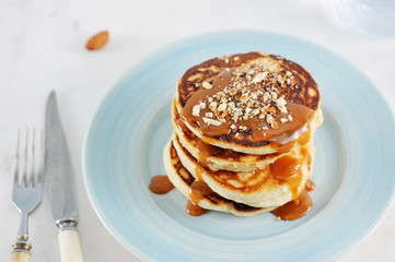 Pancakes with caramel and nuts. Several pancakes are lined with a pile, poured with caramel syrup, sprinkled with nutmeg almonds. Next to the plate are cutlery. Close-up. 