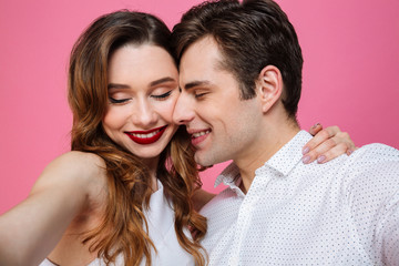 Portrait of young romantic man and woman hugging and enjoying time together, isolated over pink background