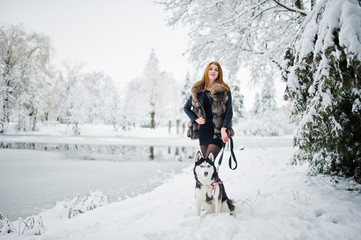 Red haired girl walking at park with husky dog on winter day.