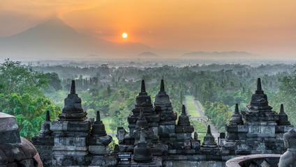 Sunrise panorama of Mount Merapi, Borobudur valey covered with mist and 9th century Stone Stupa at Borobudur Buddhist temple (UNESCO World Heritage Site). Magelang, East Java, Indonesia - obrazy, fototapety, plakaty