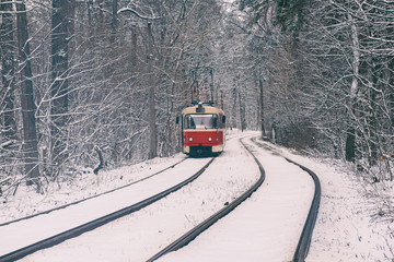 Red tram moving on the rails in the winter snowy forest, seasonal background