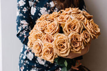 Young woman holding a big beautiful blossoming cappuccino roses bouquet on the grey wall background, cropped photo