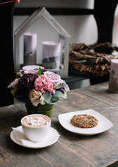 Delicious hot chocolate in a ceramic tea cup with sweet cookies and flower arrangement on the rustic wooden table background