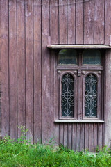 Old vintage window on a wooden house. brown background. Green grass at the bottom.