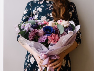 Young woman holding a big beautiful blossoming flower bouquet on the grey wall background, cropped photo