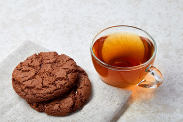 Top view close up picture of tea in transparent cup with cookies on a cotton napkin on white background, selective focus