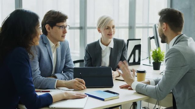 Businessman discussing future business project with male and female colleagues sitting at the table in modern office