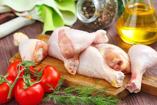 Raw chicken legs with spices and vegetables on a cutting board