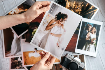 Printed wedding photos with the bride and groom, a vintage black camera and woman hands with photo - obrazy, fototapety, plakaty