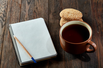 Cup of tea with cookies, workbook and a pencil on a wooden background, top view