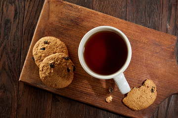 Cup of tea with cookies on a cutting board on a wooden background, top view