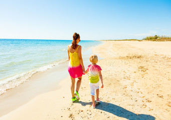 modern mother and child in colorful clothes on beach walking