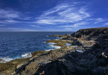 Fototapeta na wymiar Felsige Meeresküste mit Lavagestein und Windwolken. 