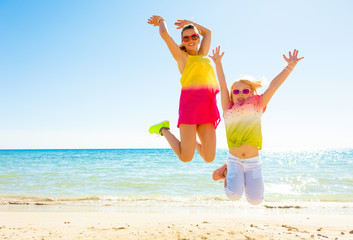 smiling trendy mother and child on seashore jumping