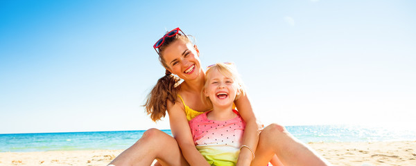 happy trendy mother and daughter sitting on beach