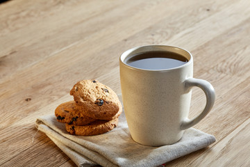 Porcelain teacup with chocolate chips cookies on cotton napkin on a rustic wooden background, top view