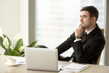 Handsome successful businessman pondering interesting idea, dreaming of company future, planning business startup financial strategy while sitting at desk in front of laptop. Positive thinking concept