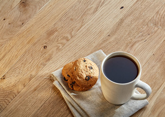 Porcelain teacup with chocolate chips cookies on cotton napkin on a rustic wooden background, top view