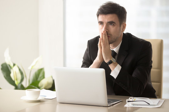 Worried company leader thinking about problem solution, pondering important question, frustrated because of difficulties in business while sitting at desk. Religious businessman praying at workplace