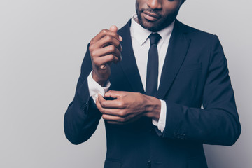 Cropped half face portrait of trendy, attractive, stunning man in black tuxedo with tie fasten button on sleeve cuffs of his white shirt, isolated on grey background