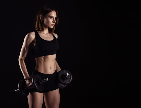 Sporty muscular female doing workout with dumbbells isolated on black background. Athletic young woman do a fitness workout with weights.