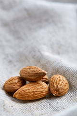 Heap of almond nuts on light tablecloth, close-up, shallow depth of field, selective focus, macro, vertical.