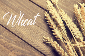 Word wheat written next to wheat flower on wooden table. Food. Concept.