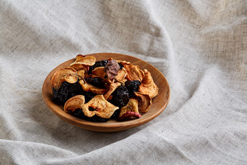 Close-up wooden plate with dried fruits on a light tablecloth