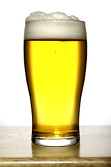 Glass of beer with white foam on wood and white background