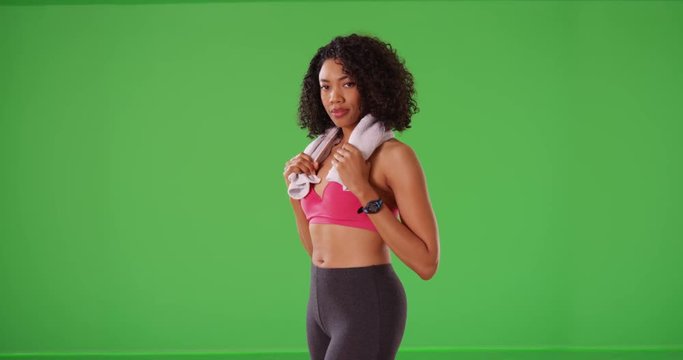 Strong and happy black woman athlete with towel on neck smiles on greenscreen. Confident young female training smiling at camera wearing active wear on green screen. 4k