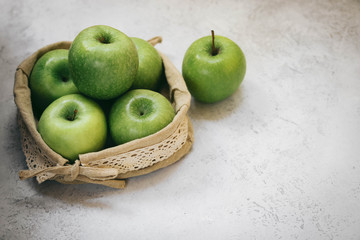 Green apples in a woven small bag on a light background