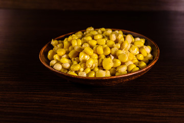 Ceramic plate with canned corn seeds on wooden table