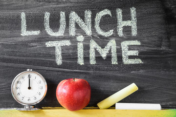 Lunch time inscription. Chalks, red apple and clock at the blackboard in classroom.  School lunch...