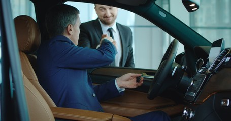 Salesman shaking hand to new owner after presentation while sitting inside new car in showroom