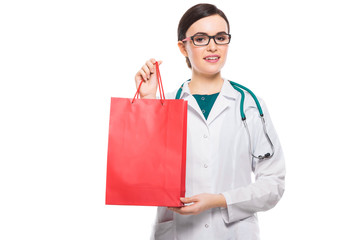 Successful young woman doctor with stethoscope offering shopping bag in white uniform on white background