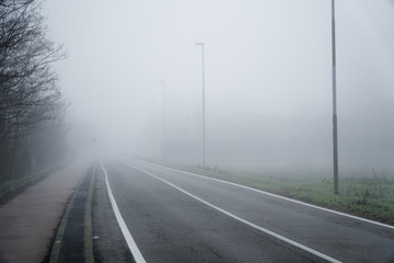Asphalt road that goes through a misty foggy dark misterious pempty fields