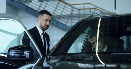 Fototapeta na wymiar Elegant salesman presenting car to potential buyer in showroom.