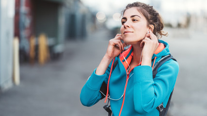 Pretty woman listening music before doing  workout, standing on the city street
