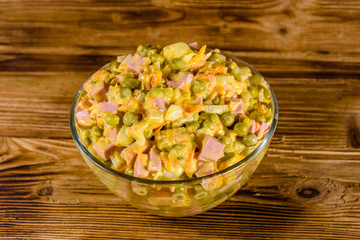 Salad with sausage, green pea, onion and carrot in glass bowl on wooden table