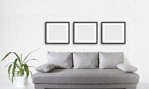Three blank frames set over modern couch, and yucca plant in white flower pot near bricks wall, interior decor mock up.