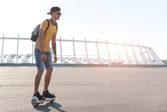 Full length side view cheerful teenager going on hoverboard at street in sunny day. Copy space
