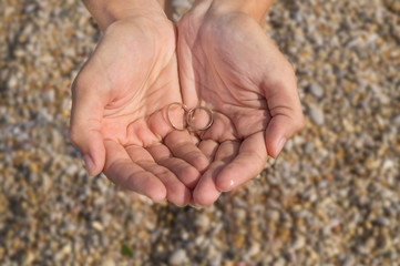 Two wedding rings in female hands on beach background