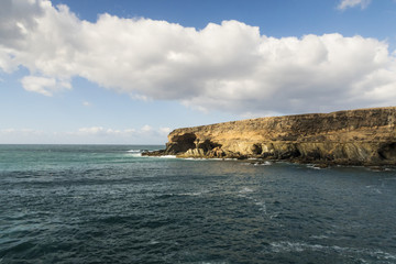 rugged coastline on Fuerteventura with turquiose water against partially clouded blue sky